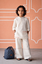 Load image into Gallery viewer, Child wearing a traditional outfit with a blue bag against a pink wall