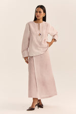 Load image into Gallery viewer, A woman modeling a light pink two-piece outfit consisting of a long-sleeve tunic top with a split neckline and a matching wide-leg skirt, photographed against a solid light beige studio background.