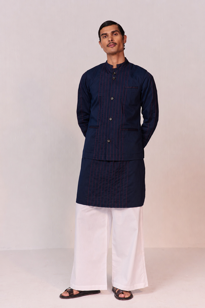 Man wearing a dark blue kurta with white pants on a light background