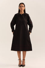 Load image into Gallery viewer, A woman modeling a black long-sleeve tunic dress with subtle red embroidered stripes near the hem and cuffs, paired with black high heels, against a plain light beige studio background.
